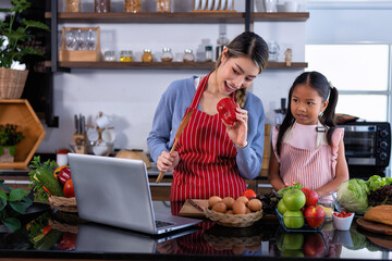 Wall Mural - Young mother teach daughter in the kitchen learn online cooking clean food from the laptop computer