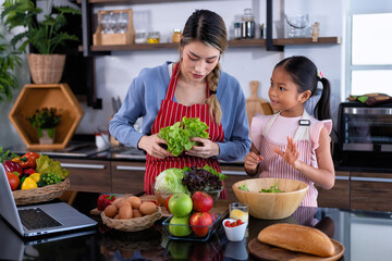 Young mother teach daughter in the kitchen learn online cooking clean food from the laptop computer