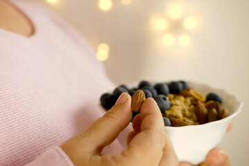 close-up female hand takes almonds on blurred background with bokeh, healthy food white cup, blueberries, nuts, almonds, peanuts , raisins, dried fruits, raw food diet, vegetarian food