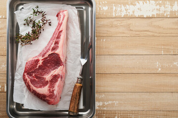 Wall Mural - Fresh tomahawk raw steak. Dry aged raw tomahawk beef steak with herbs and salt on old wooden background. Preparing to grill.  Top view and copy space.