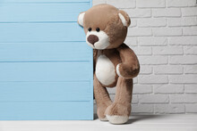 Cute Teddy Bear Near Light Blue Wooden Wall Against Brick Background, Space For Text