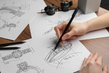 Jeweler drawing sketch of elegant ring on paper at wooden table, closeup