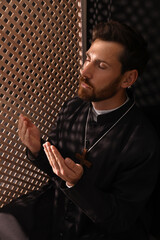 Wall Mural - Catholic priest in cassock praying to God in confessional booth