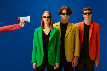 Sticker - Portrait of young people wearing colorful jackets standing near loudspeaker over blue background