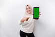 © Reezky - A happy Asian Muslim woman wearing a headscarf, showing her phone screen, isolated by white background