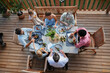 © Halfpoint - Top view of 3 generations family eating at barbecue party dinner on patio, people sitting at table on patio with grill.