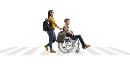 Wall Mural - Full length profile shot of a female student pushing a friend in a wheelchair at a pedestrian crossing