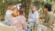 Small Asian group of people sit in a close circle and talk to a therapist in park. Smile people sharing story happy speak diverse people sitting in circle at group therapy session with psychologist.