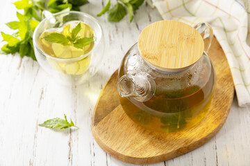 Wall Mural - Cup and teapot of fresh natural herbal tea with fresh mint leaves on rustic wooden table. Copy space.