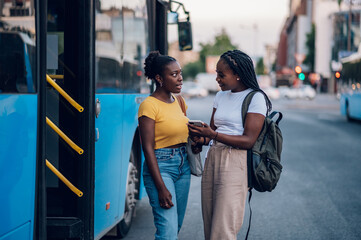 Wall Mural - Couple of african american woman talking while waiting on a bus stop