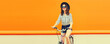 © rohappy - Summer image of happy smiling young woman with bicycle looking away on orange background, banner blank copy space for advertising text