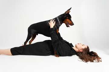 A young beautiful Doberman with a chain around his neck and his owner, elegant girl in a long black coat and bright red lipstick. Isolated on a white background.