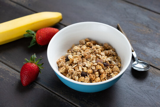 Dry granola in a bowl on wooden table. Healthy breakfast cereals, baked oat honey granola with raisins