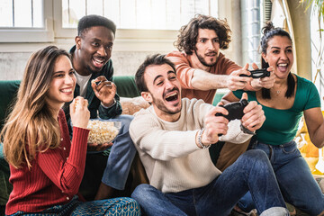 Happy multi ethnic friends sitting on sofa playing video games - Cheerful generation z group having fun with modern technology videogames - Hobby and tech concept