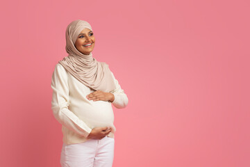 Wall Mural - Pregnant muslim woman in hijab embracing her belly and looking away