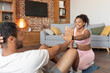 © Prostock-studio - Smiling young black female helping male athlete in sportswear doing abs exercises on floor in living room