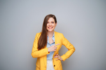 Wall Mural - Happy woman in yellow jacket on gray background pointing finger at side.