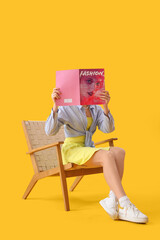 Poster - Young woman reading magazine in wooden armchair on yellow background