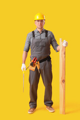 Canvas Print - Mature carpenter with hacksaw and wooden plank on yellow background