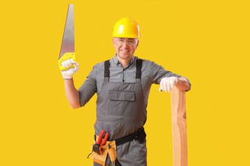 Canvas Print - Mature carpenter with hacksaw and wooden plank on yellow background