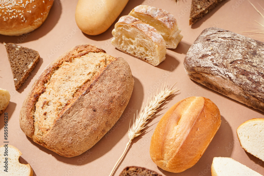 Fresh loaves of different bread and wheat ears on brown background