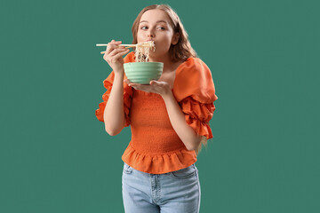 Young woman eating Chinese noodles on green background