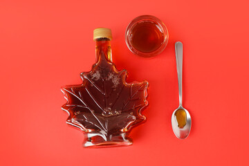 Bottle, spoon and glass of tasty maple syrup on red background