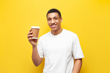 Wall Mural - young african american guy in white t-shirt holds and recommends coffee in paper cup on yellow background