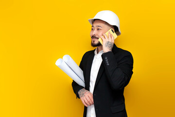 Wall Mural - asian foreman in black suit with papers and projects is talking on the phone on yellow isolated background