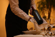 © New Africa - Butler holding bottle of wine near table in restaurant, closeup