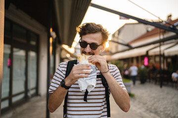 one man young adult modern caucasian male in the city in sunny day walk and eat sandwich fast food c