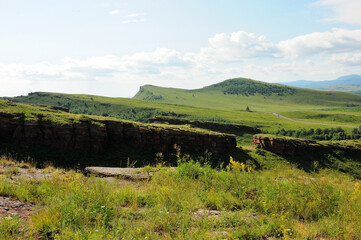 Breaks in the walls of an ancient sanctuary going along the top of a bare hill in a picturesque summer valley.