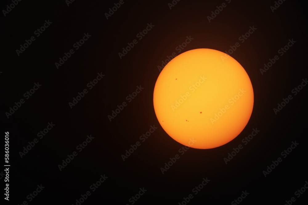 Orange sun on a black background. Big yellow-orange sun with sunspots photographed through a telescope filter on a black background with copy space. selective focus