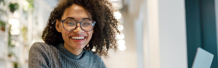 Smiling african woman freelancer working laptop while sitting in coworking and looking at camera