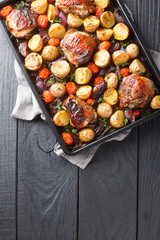 Sticker - Delicious homemade chicken thighs baked with potatoes, garlic, onions and tomatoes in balsamic vinegar close-up on a black baking sheet on a wooden table. Vertical top view from above