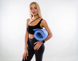 © oleg_ermak - Caucasian woman with long blond hair in black sportswear hold yoga mat or mat for fitness poses on a white background and shows perfect body. Personal care and sports at home.