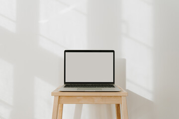 Wall Mural - Laptop computer with blank screen and sunlight shadows on the wall. Minimal styled website, online shop, store, social media template with mockup copy space