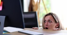 Scared Woman Peeks Out From Under Table Looking At Screen