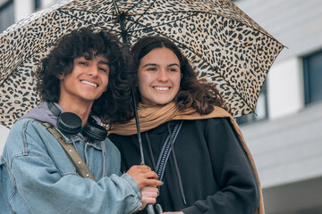 Wall Mural - couple of young teenagers with umbrellas in the street