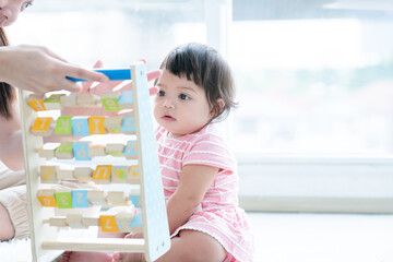 Selective focus on Caucasian cute 7 months daughter toddler baby face looking and playing with alphabet blocks toy, sitting on floor with mother at home. Development, education, growth child care