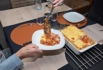  a woman serving hot homemade lasagna on plates to a family member sitting