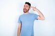 © Jihan - Young caucasian man wearing blue T-shirt over white background foolishness around shoots in temple with fingers makes suicide gesture. Funny model makes finger gun pistol