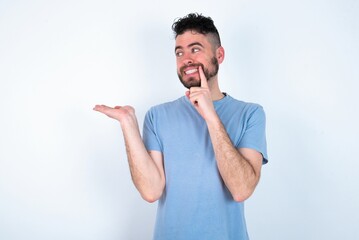 Wall Mural - Positive Young caucasian man wearing blue T-shirt over white background advert promo touch finger teeth