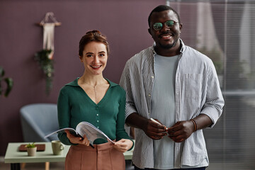 Waist up portrait of two people looking at camera and smiling while standing in modern office setting