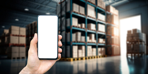 Warehouse with a hand holding an empty smartphone. Blurred industrial warehouse with goods and products. Logistics, business, delivery, services concept 