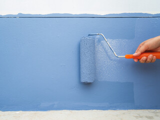 Bare hand holding the handle of the paint roller. pastel blue dip Rolled paint over the old wall. to repair old deteriorated walls Renovation and home decoration