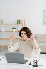 Wall Mural - young sign language teacher showing alphabet letters with hands during online lesson on laptop at ho