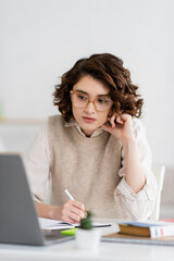 Wall Mural - pretty student in glasses taking notes while learning foreign language and watching online lesson on