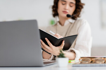 Wall Mural - language teacher writing in notebook near laptop during online lesson.