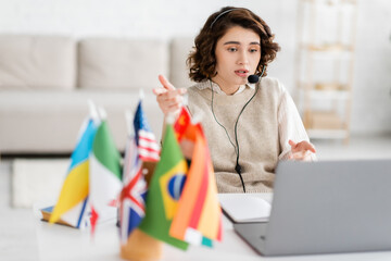 Wall Mural - language teacher in headset pointing with fingers while talking during video chat on laptop near blu